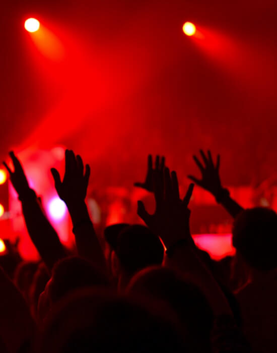 Um grupo de pessoas erguem as mãos em uma apresentação musical, sob uma iluminação avermelhada.