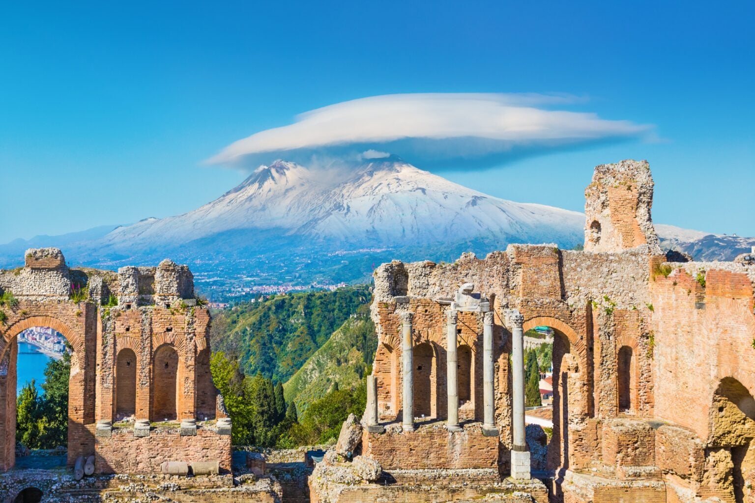Ancient Greek theatre in Taormina on background of Etna Volcano, Italy. Taormina located in Metropolitan City of Messina, on east coast of island of Sicily.