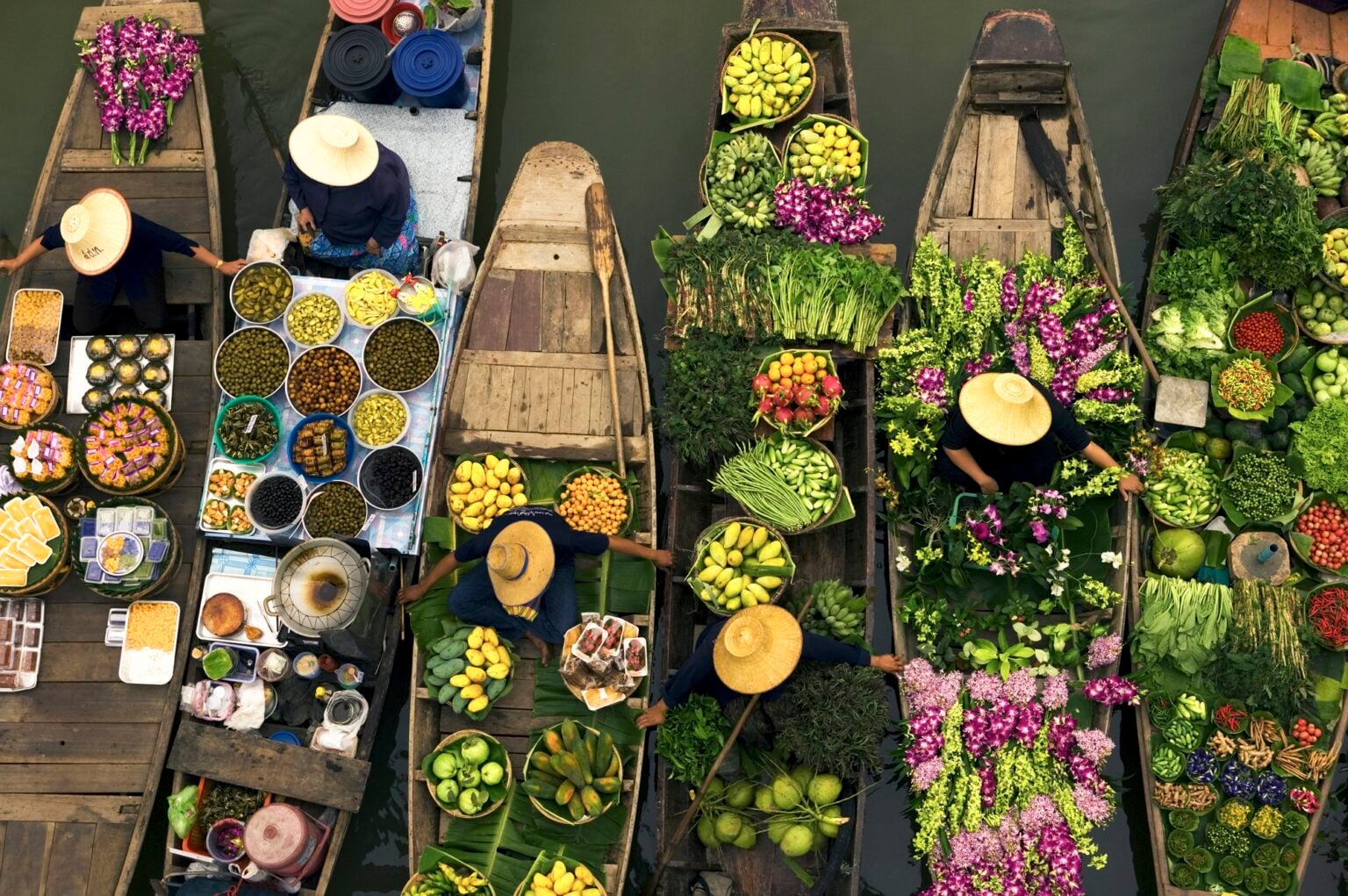 Aerial view of a floating market on a canal in Bangkok, local boats laden with fresh food, moored close together.