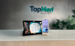 Profissional realizando exame de termografia com AuroraCare TopMed mostrando imagem térmica colorida das mamas em smartphone durante rastreamento preventivo