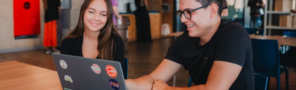 Homem e mulher sorrindo ao acessar o Portal do Fornecedor no notebook, representando automação, comunicação e visibilidade do processo do pedido ao pagamento com o V360.